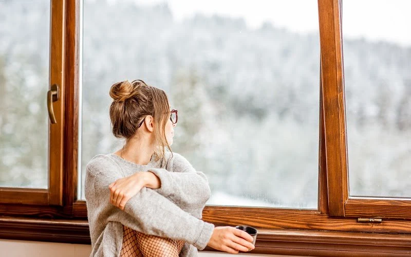 Une femme qui s'assoie et qui regarde par la fenêtre avec un double vitrage et un cadran en bois.